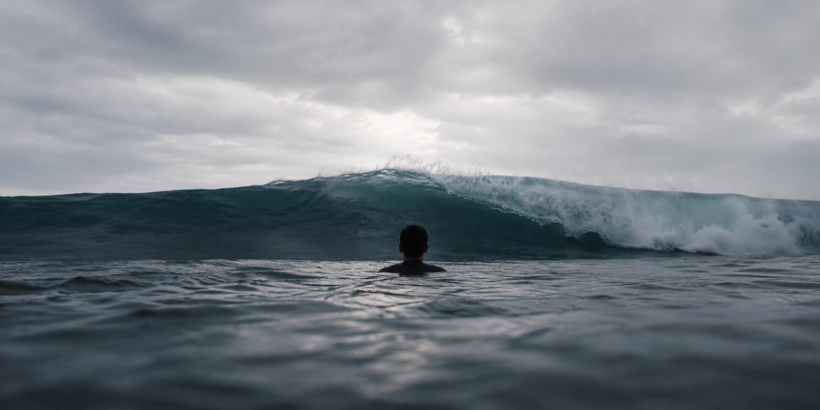 A person in the ocean, neck-deep, facing a wave about to break